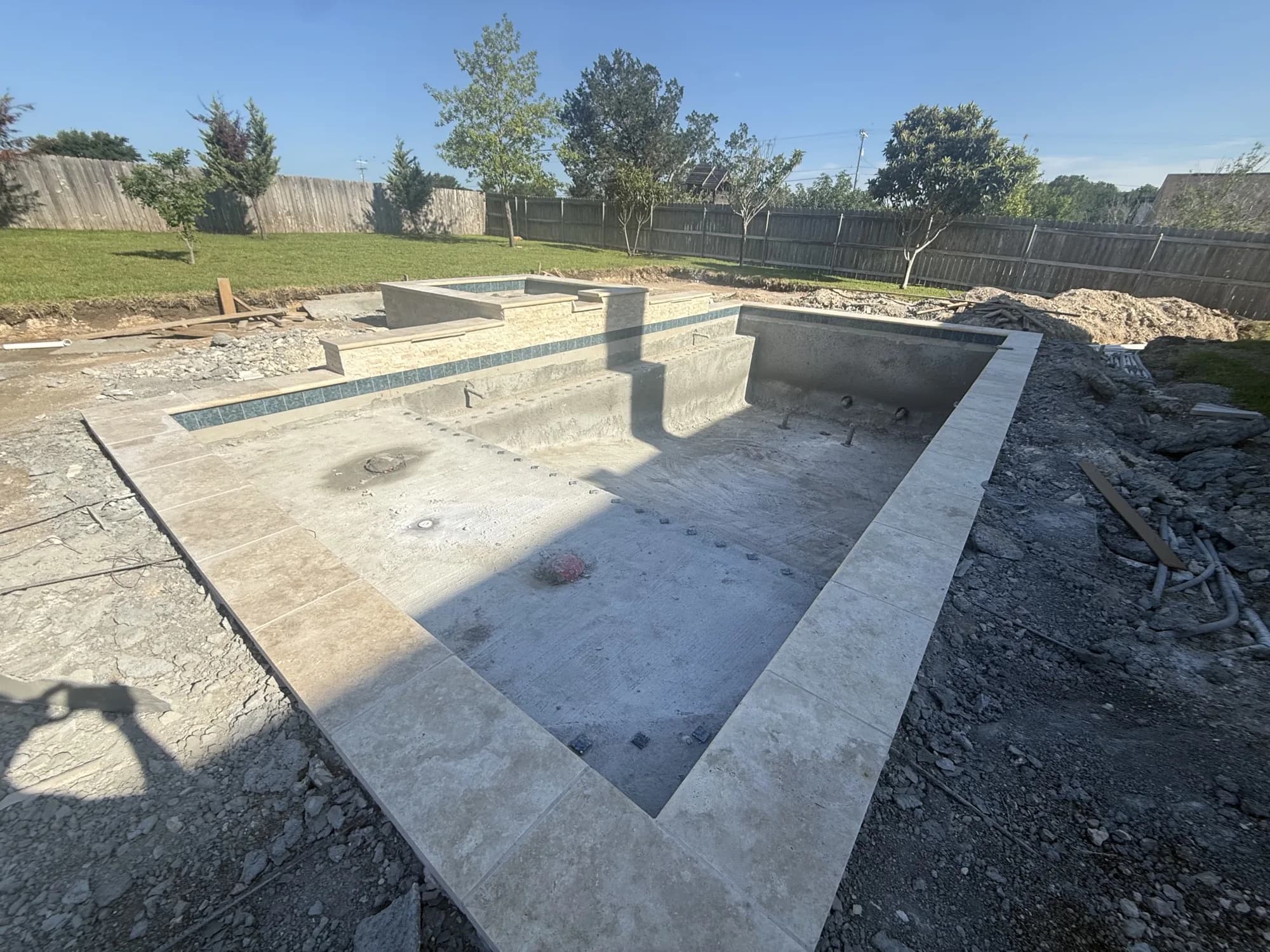 Gunite pool shell with raised spa, waterline tile, and travertine coping before plaster